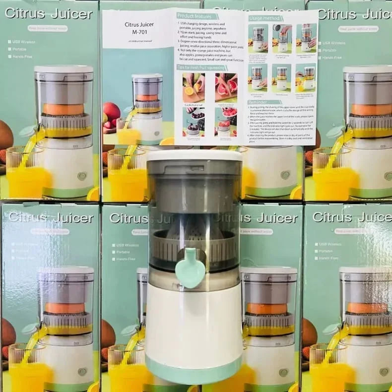 A countertop citrus juicer appliance centered in front of multiple retail boxes labeled Citrus Juicer. The juicer has a white body with a translucent gray top chamber and a pale mint green spout.