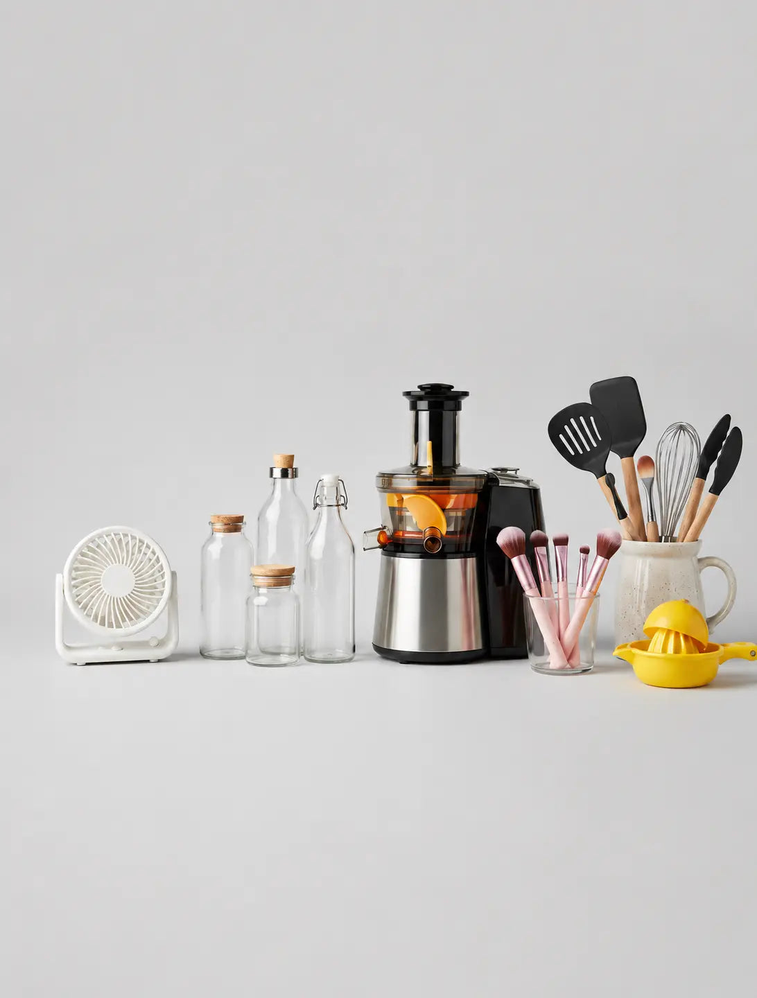 Daily Choice PK mobile banner — smart everyday products. A styled product lineup on a light gray background featuring a stainless steel and black countertop juicer with an orange slice, surrounded by clear glass bottles, a small white fan, makeup brushes in a cup, and kitchen utensils in a mug.